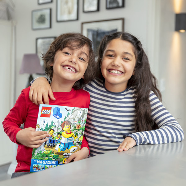 two smiling children with one holding LEGO magazine.